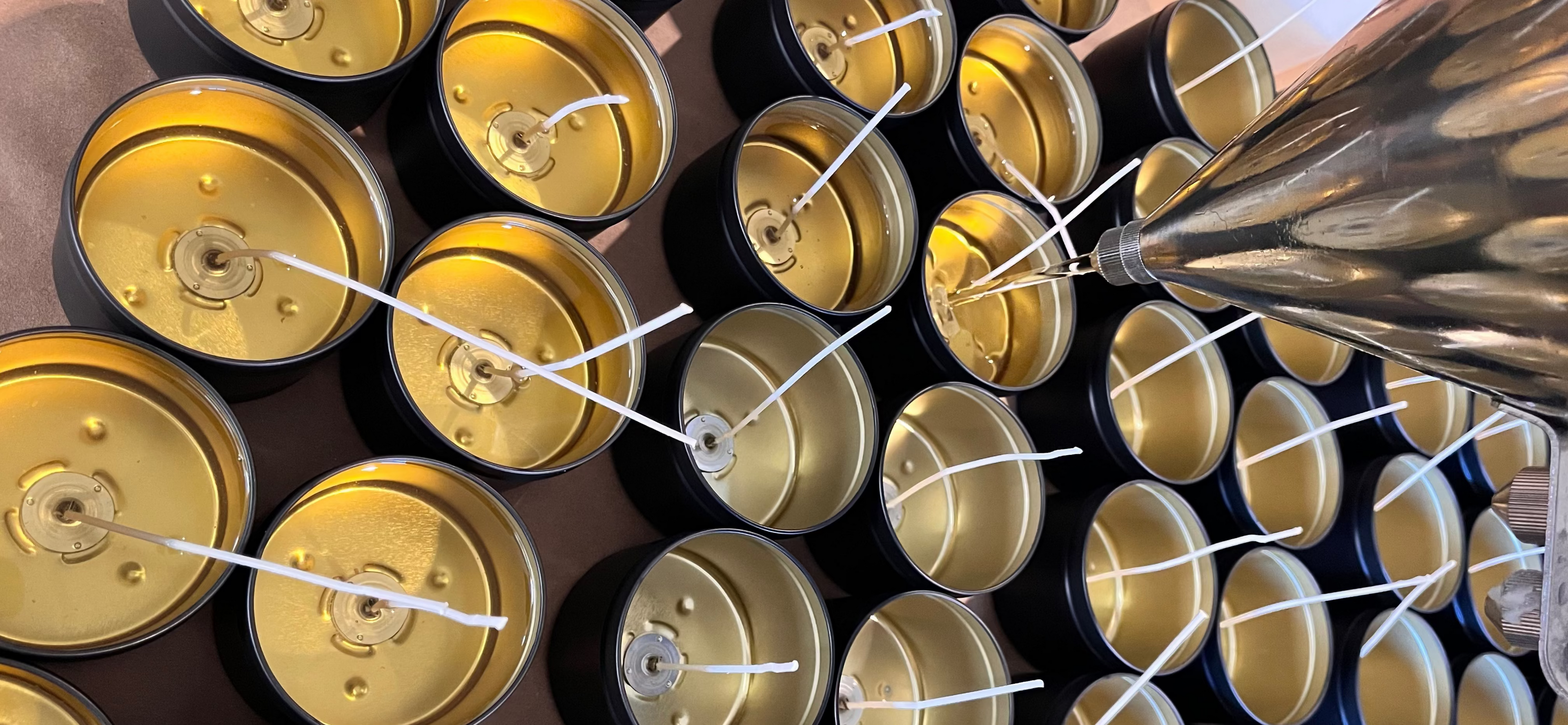Candle-making process with a funnel pouring wax into small candle tins.